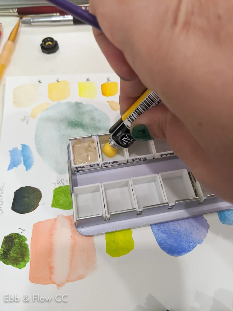 filling a watercolor palette with paint from a tube