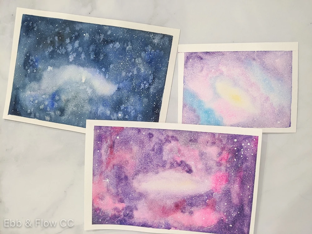 3 different paintings of galaxies using watercolor paint