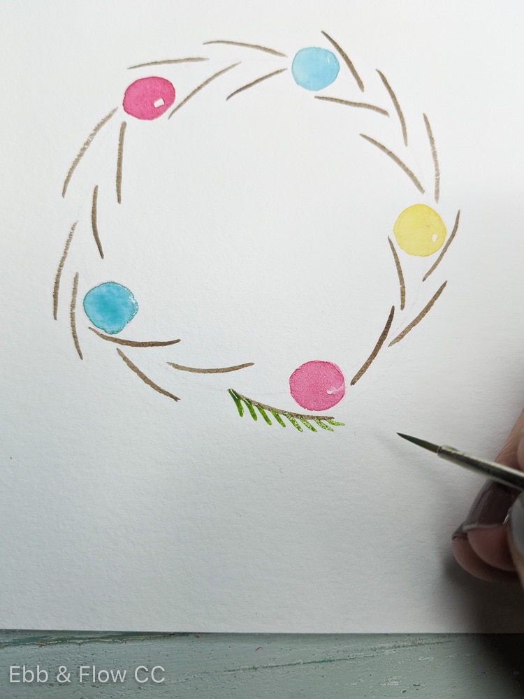adding pine needles to stems of painted wreath