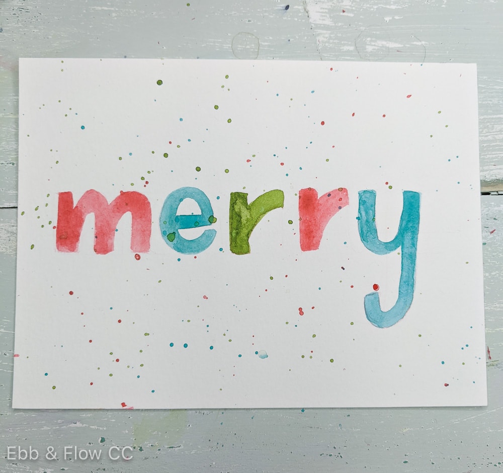 paint spatter on hand lettered card that says "merry"