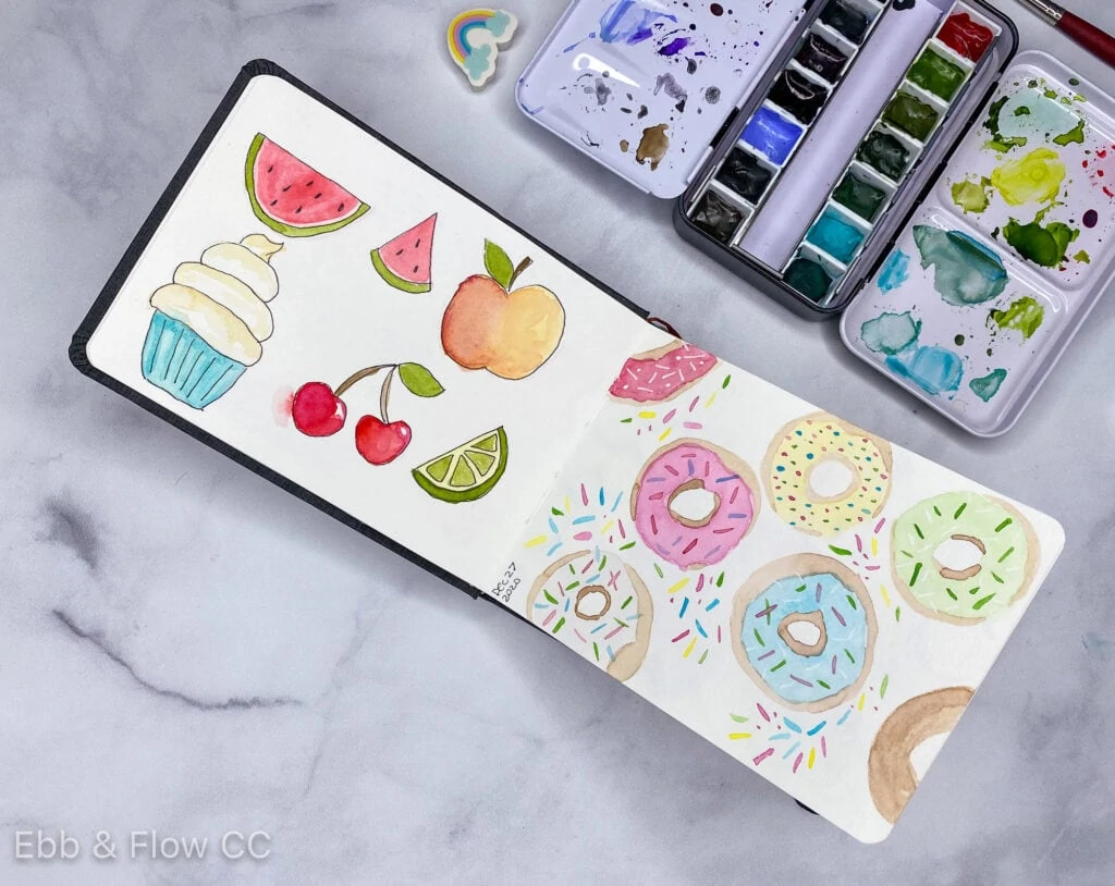 open sketchbook with paintings of fruit and donuts