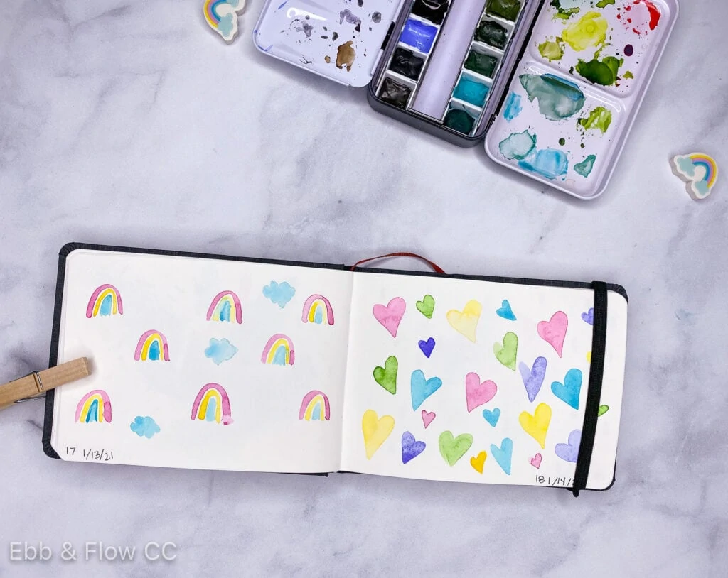 sketchbook with watercolor paintings of hearts and rainbows
