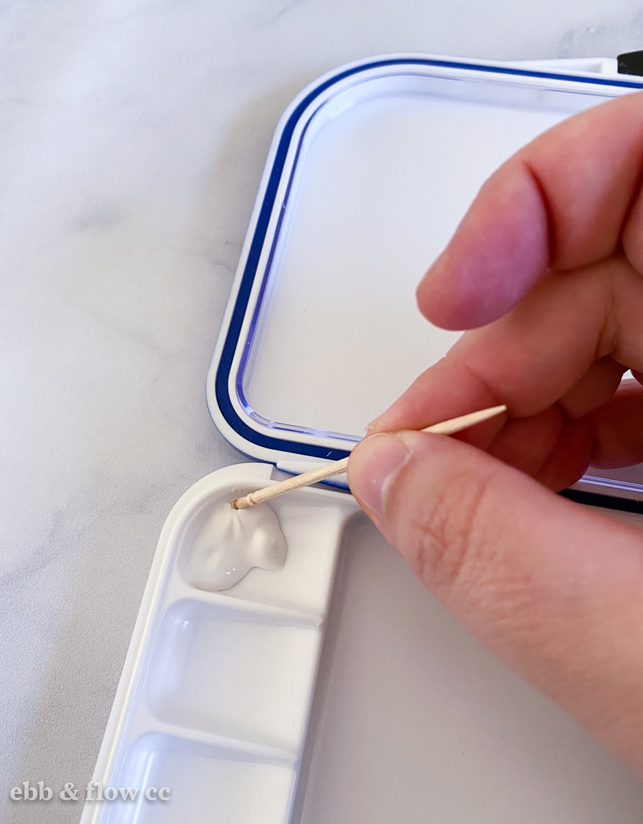 hand spreading white paint with toothpick