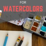 pencils, watercolor paint and paper on desk